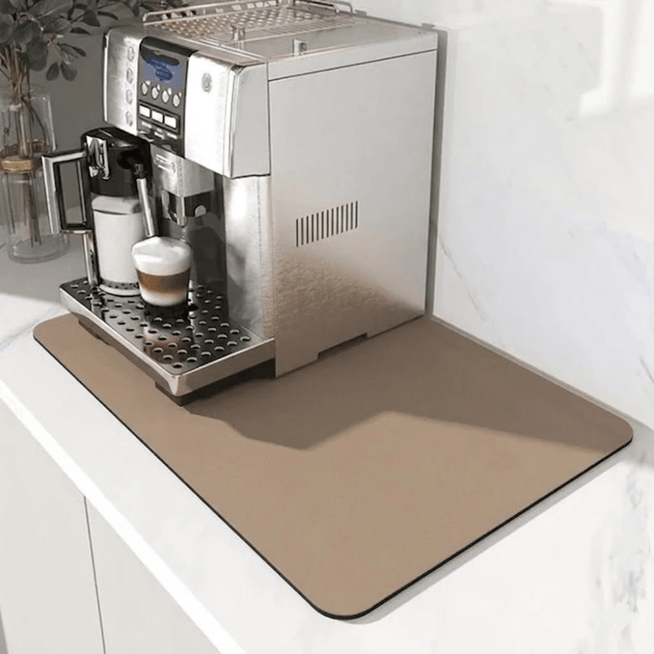 Beige måtte under en kaffemaskine på en hvid bordplade, med en latte i glasset under mælkeskummeren. 7