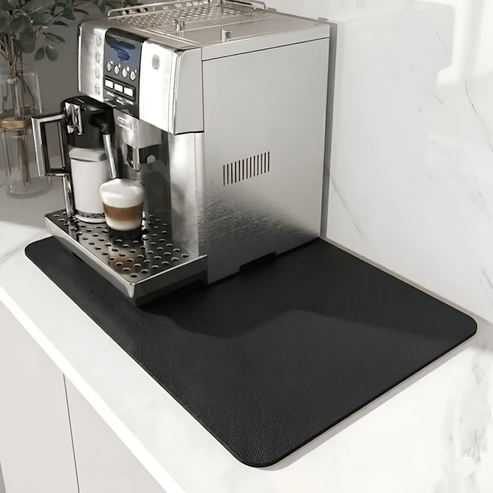 Sort måtte med let skindlignende overflade under en espressomaskine på en hvid marmorbordplade. 9