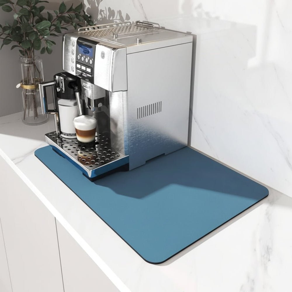 Blå rektangulær måtte med afrundede hjørner under en espressomaskine på en hvid marmorbordplade, set skråt fra siden. 1