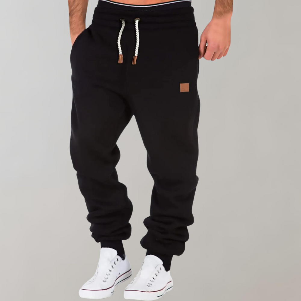 Model i sorte joggingbukser med hvidt snøre og læderlabel, set forfra med hvide sneakers 1